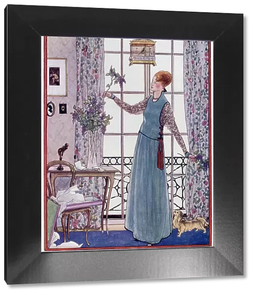 A lady in a pinafore dress artistically arranges lilac coloured blossom in a tall, narrow stemmed glass vase, watched on by her pekinese dog. Date: 1915