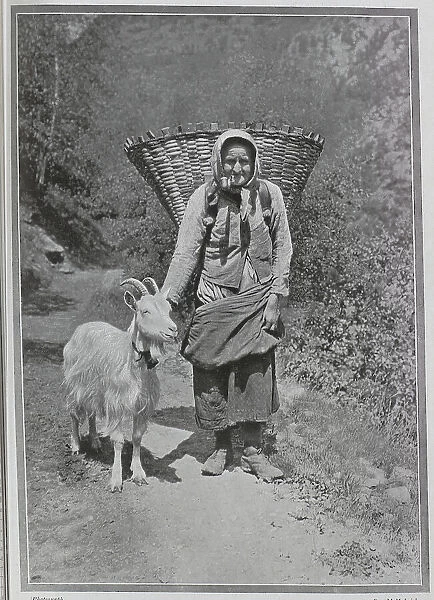 Alpine woman with headscarf, pipe, large basket and goat, outdoor scenic photograph. Captioned Beauty and the Beast, and an Alpine Discovery'. Date: 1910