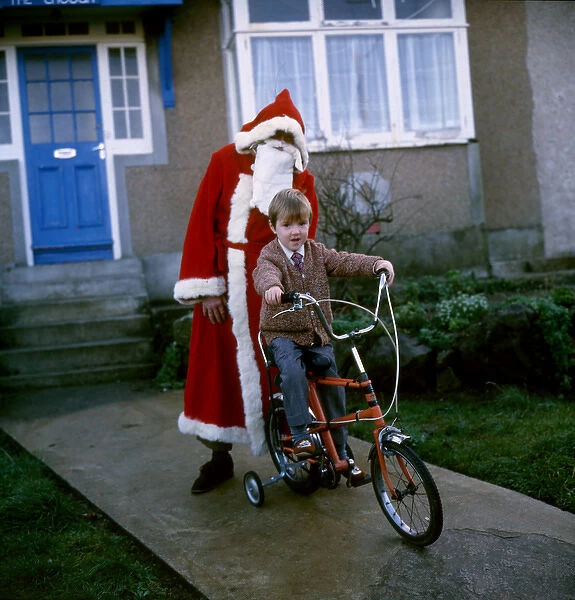 Father Christmas stands behind boy on bike