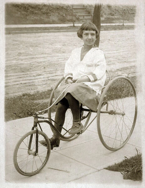 Girl riding a vintage peddle tricycle along the sidewalk
