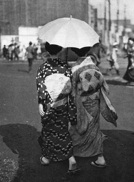 Two Japanese women walk holding a parasol