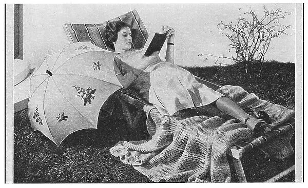 Model reading on a garden lounger with an umbrella, wearing very thick silk stockings, advertising patterns for an embroidered sunshade and knitted blanket. Date: 1935