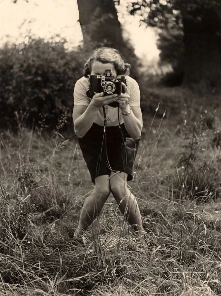 Smile. A woman with a camera adopts a photographers pose for - another photographer