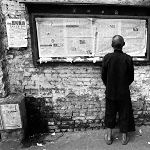 A man readis a newspaper on a noticeboard in a Canton street
