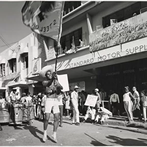 A young man in shorts dances and waves a flag about at the Port of Spain Carnival, Trinidad, West Indies. Date: 1968