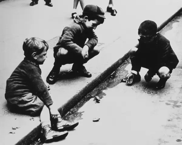Three boys playing marbles in the gutter