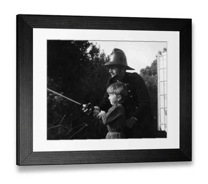 Framed Print : Fireman showing boy how to use a hose Framed Print : Fireman showing boy how to use a hose