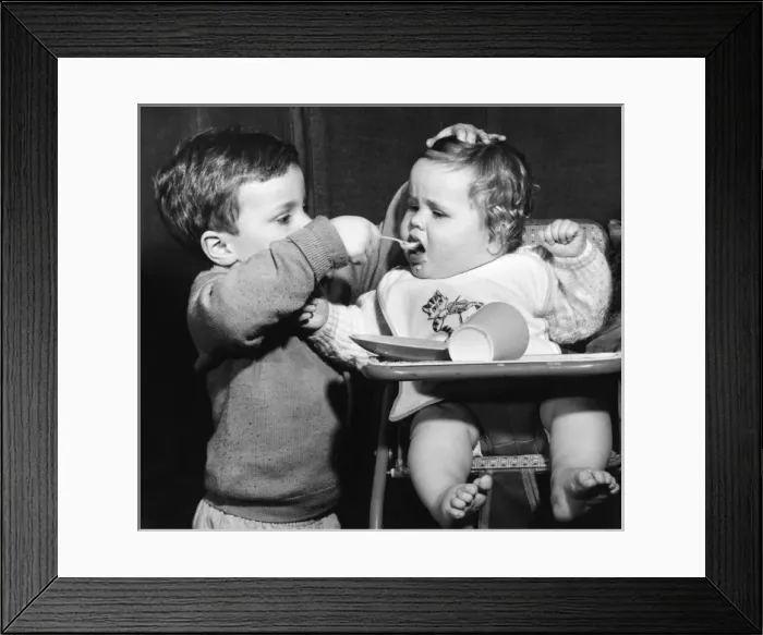 Framed Print : Boy feeding baby in a high chair Framed Print : Boy feeding baby in a high chair