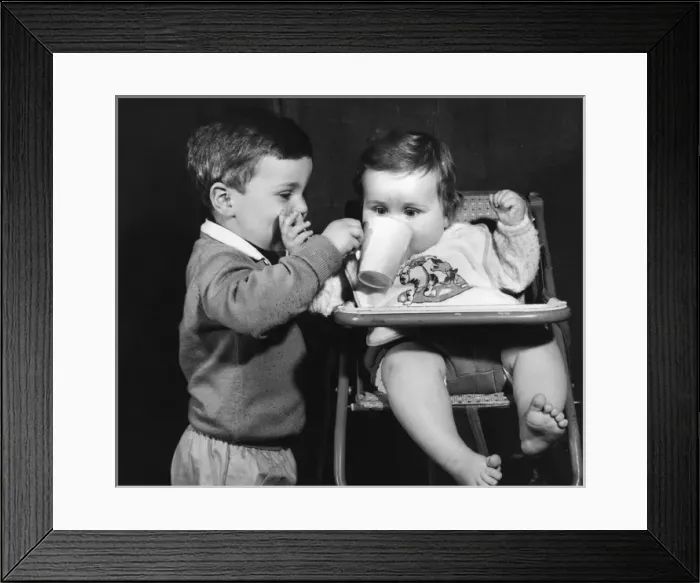 Framed Print : Boy giving drink to a baby in a high chair Framed Print : Boy giving drink to a baby in a high chair