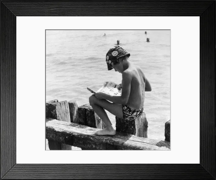 Framed Print : Boy sitting on breakwater reading a comic Framed Print : Boy sitting on breakwater reading a comic