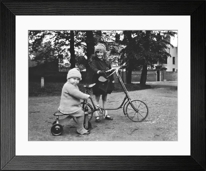 Framed Print : Girl and toddler riding a bicycle and a tricycle Framed Print : Girl and toddler riding a bicycle and a tricycle