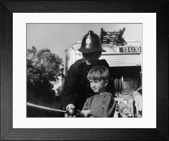 Framed Print : Fireman showing boy how to use a hose Framed Print : Fireman showing boy how to use a hose