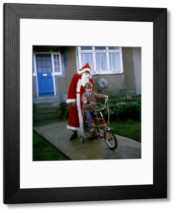 Framed Print : Father Christmas stands behind boy on bike Framed Print : Father Christmas stands behind boy on bike