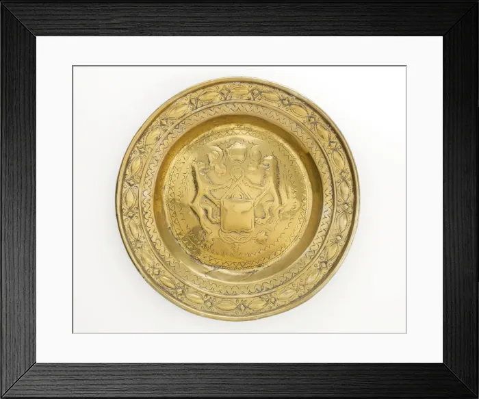 Framed Print : Almsdish in brass with a central hammered design featuring two lions flanking a shield Framed Print : Almsdish in brass with a central hammered design featuring two lions flanking a shield