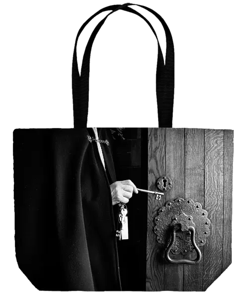 A priest wearing a black cloak unlocks the oak door of a chu