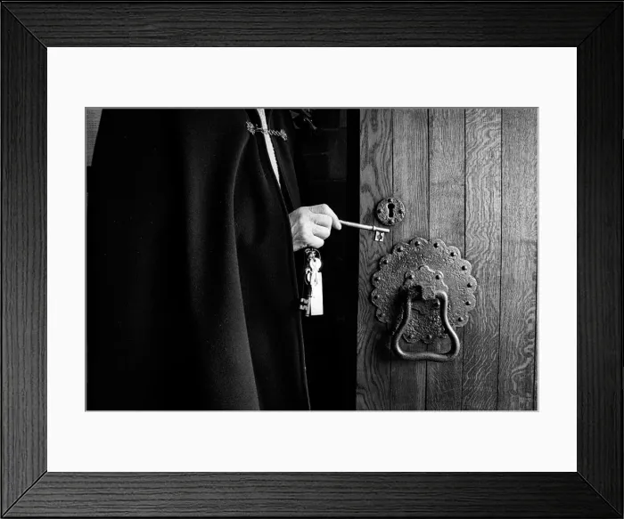 Framed Print : A priest wearing a black cloak unlocks the oak door of a chu Framed Print : A priest wearing a black cloak unlocks the oak door of a chu