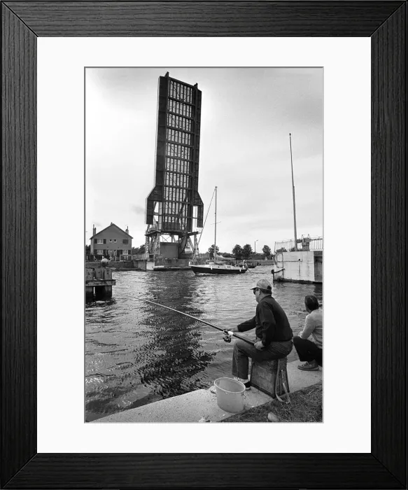 Framed Print : Fishermen on towpath as yacht passes raised Pegasus Bridge Framed Print : Fishermen on towpath as yacht passes raised Pegasus Bridge