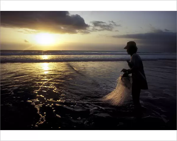 A Balinese fisherman pauses to look at the sunset