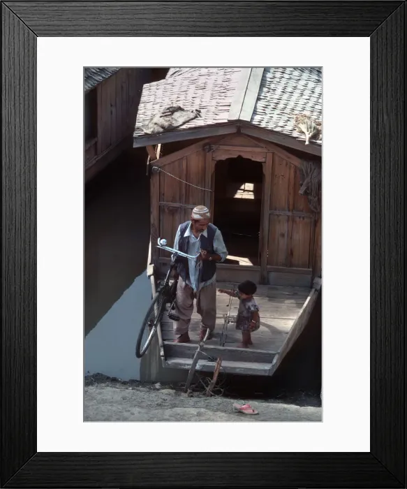 Framed Print : Kashmir, Dal Lake. A man lifts his bicycle off his boat Framed Print : Kashmir, Dal Lake. A man lifts his bicycle off his boat
