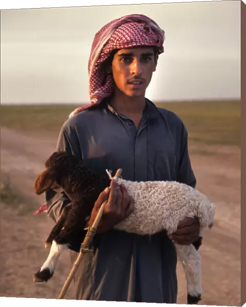 Syrian bedhouin shepherd boy holds a small lamb in his arms