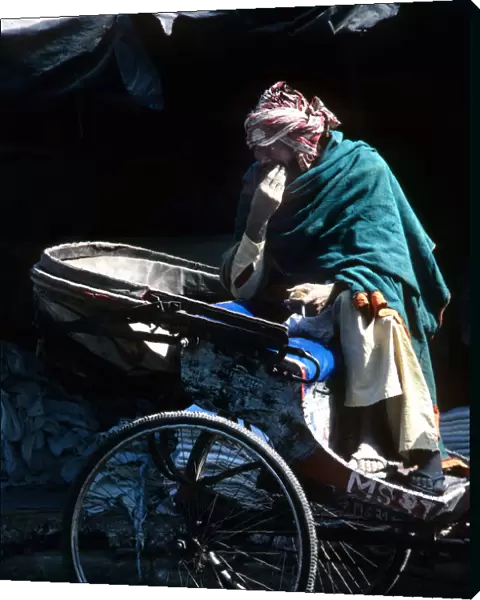 A ragged driver sits on his cycle rickshaw, India