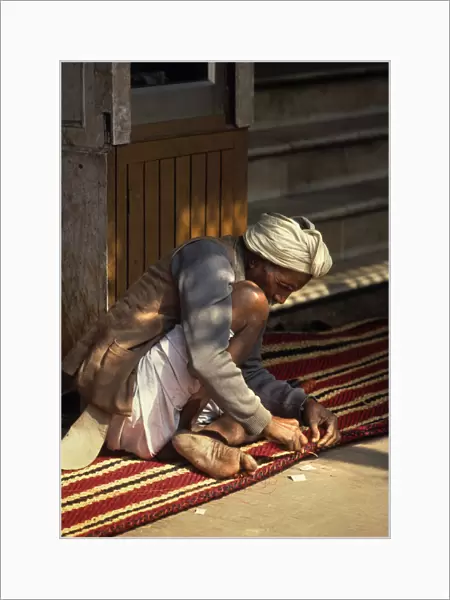 Carpet maker stitches the hem of a striped carpet, Rajasthan
