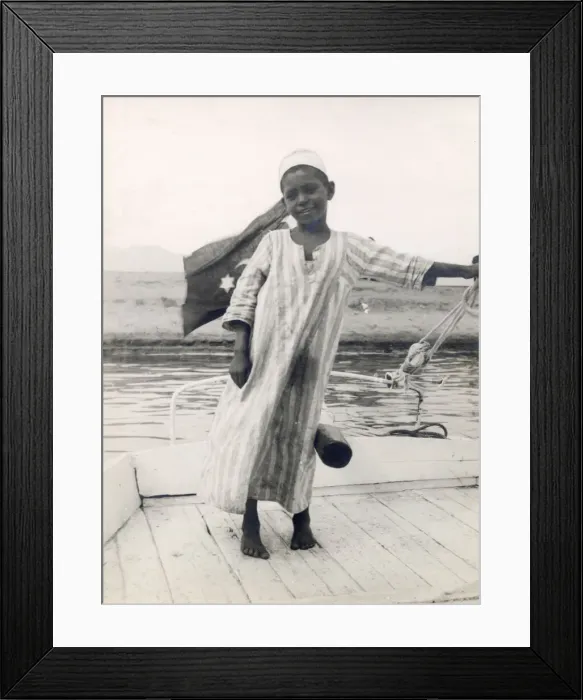 Framed Print : The little son of a ferryman at Luxor, Egypt, steers his fathers boat with his leg Framed Print : The little son of a ferryman at Luxor, Egypt, steers his fathers boat with his leg