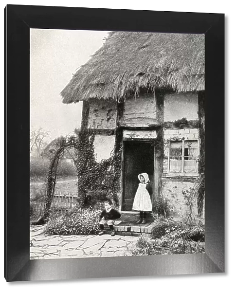 Boy and girl outside a thatched cottage, Worcestershire