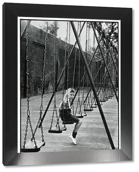 Young boy alone on a playground swing 1939