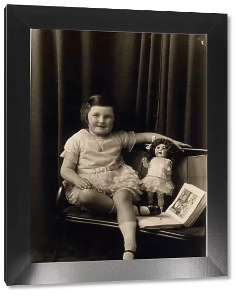 Studio photograph of a little girl pictured with a doll and picture book