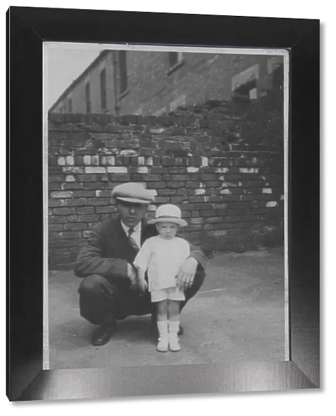 A father poses with his little boy in a back street. Date: 1920s