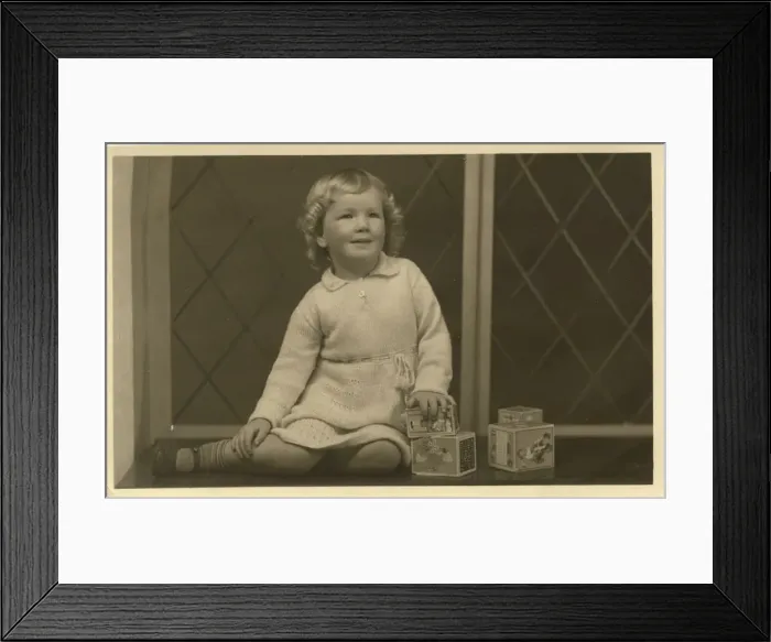 Framed Print : A little girl grins for her photograph, alongside some toy building blocks Framed Print : A little girl grins for her photograph, alongside some toy building blocks