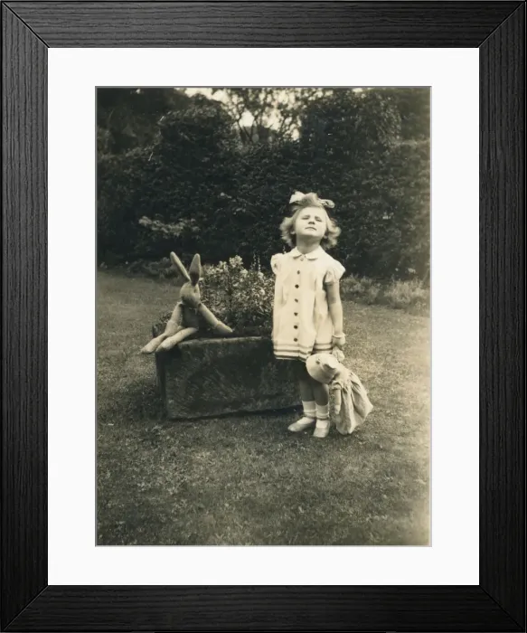 Framed Print : A little girl stands to attention and grimaces for the camera in a garden holding a doll Framed Print : A little girl stands to attention and grimaces for the camera in a garden holding a doll