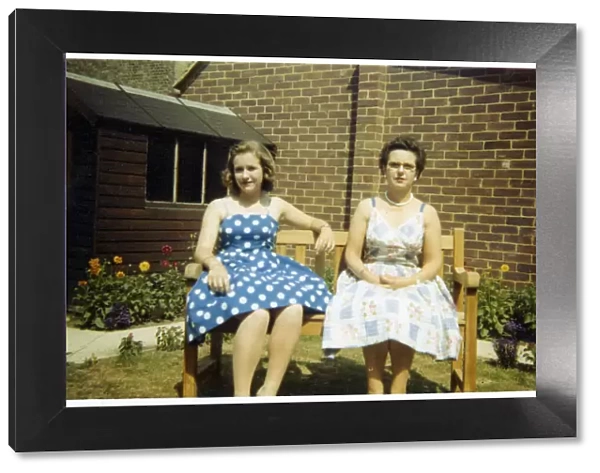 Mother and daughter in summer dresses on a garden bench