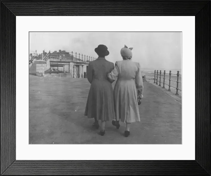 Framed Print : Back view of two ladies walking along an unidentified sea front arm in arm. Date: c Framed Print : Back view of two ladies walking along an unidentified sea front arm in arm. Date: c