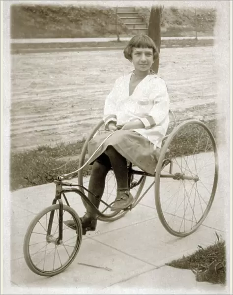Girl riding a vintage peddle tricycle along the sidewalk