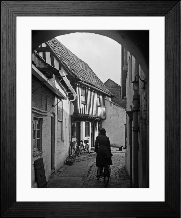 Framed Print : Woman cycling along path between houses Framed Print : Woman cycling along path between houses
