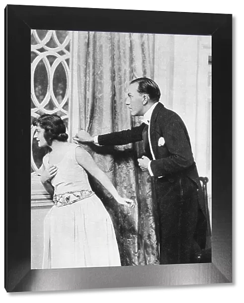 Noel Coward acts in his own play with Ann Trevor. Dressed for dinner, they peer anxiously out of a window. Date: 1923