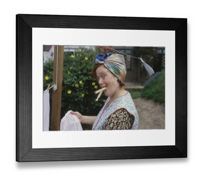 Framed Print : A housewife with a mouthful of clothes pegs strikes a pose as she hangs out the washing! Date: 1940s (re-enactment) Framed Print : A housewife with a mouthful of clothes pegs strikes a pose as she hangs out the washing! Date: 1940s (re-enactment)