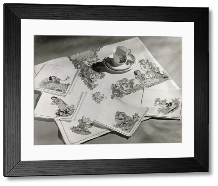 Framed Print : A Snow White and the Seven Dwarfs cup and saucer, with matching table cloth and table napkins or serviettes. Date: 1930s Framed Print : A Snow White and the Seven Dwarfs cup and saucer, with matching table cloth and table napkins or serviettes. Date: 1930s