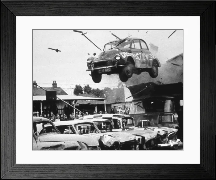 Framed Print : A stunt car flies through the air over a row of other cars, watched by spectators. Date: 1960s Framed Print : A stunt car flies through the air over a row of other cars, watched by spectators. Date: 1960s