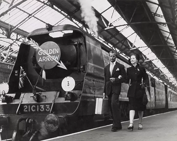 A couple walk arm in arm on a railway platform, beside the luxury locomotive the Golden Arrow, which linked London to Dover, where passengers caught the ferry to Calais, France. Date: 1947