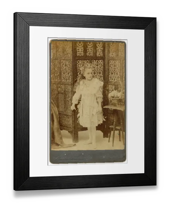 Framed Print : Young girl in studio photo with ornately carved wooden screen behind her Date: circa 1910s