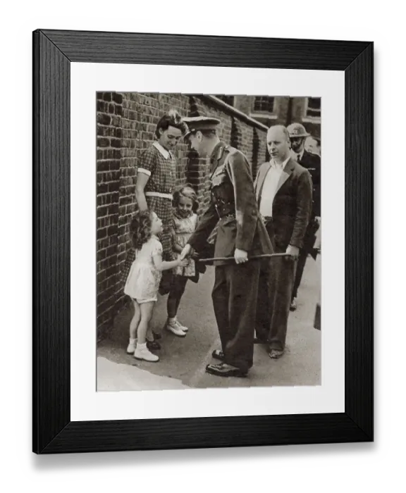Framed Print : King George VI's visit to the bomb-shattered East End of London in September 1940: shaking hands with the little daughter, Joan Miles, of the caretaker of a school which was bombed. Date: September 1940