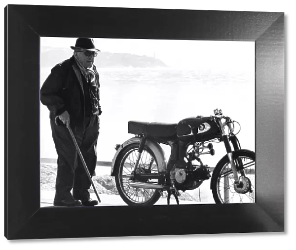 Old man standing next to a motorcycle near a beach