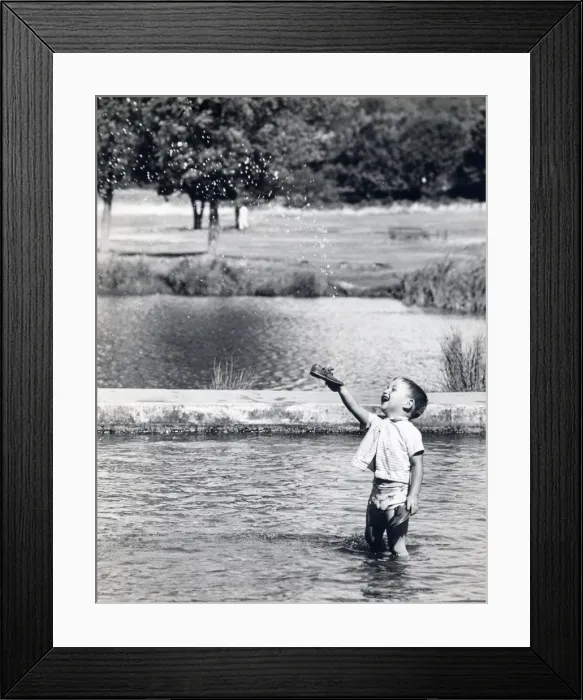 Framed Print : Little boy paddling in a pond holds up his new shoes Framed Print : Little boy paddling in a pond holds up his new shoes