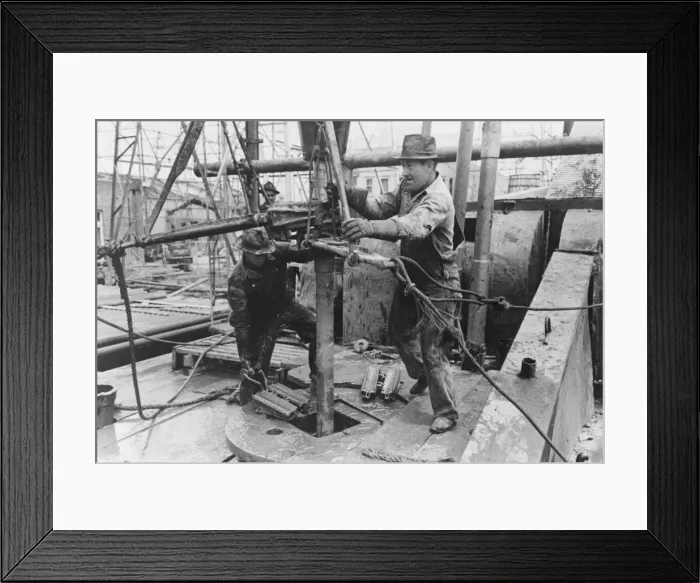 Framed Print : Oil field workers adding a length of pipe to drill stream by