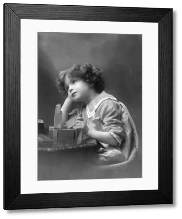 Framed Print : A curly-haired boy playing with wooden building bricks Framed Print : A curly-haired boy playing with wooden building bricks