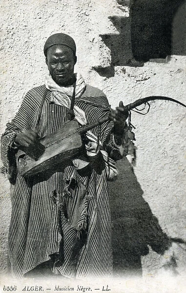 Algeria - African Gnawa Musician playing a traditional sintir, also known as the guembri, gimbri or hejhouj, a three-stringed skin-covered bass plucked lute. Date: circa 1910s