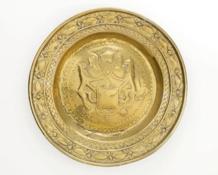 Framed Print : Almsdish in brass with a central hammered design featuring two lions flanking a shield Framed Print : Almsdish in brass with a central hammered design featuring two lions flanking a shield